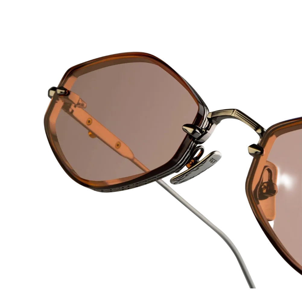 Close-up of a pair of sunglasses with dark brown translucent frames, brown tinted lenses, and a thin silver metal temple arm on a white background.