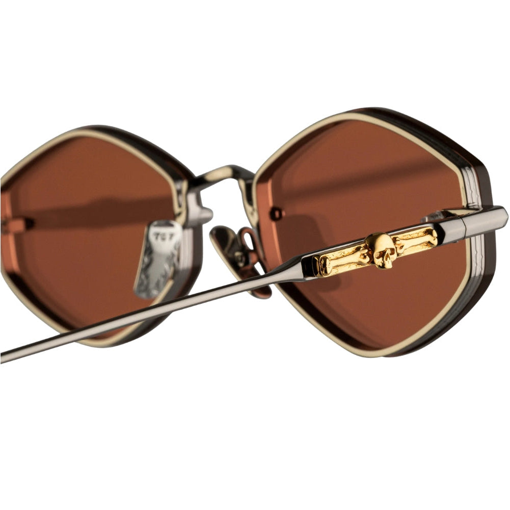 Close-up of a pair of sunglasses with large brown lenses, a dark frame, and gold-toned metal details on the hinge, shown against a plain white background.