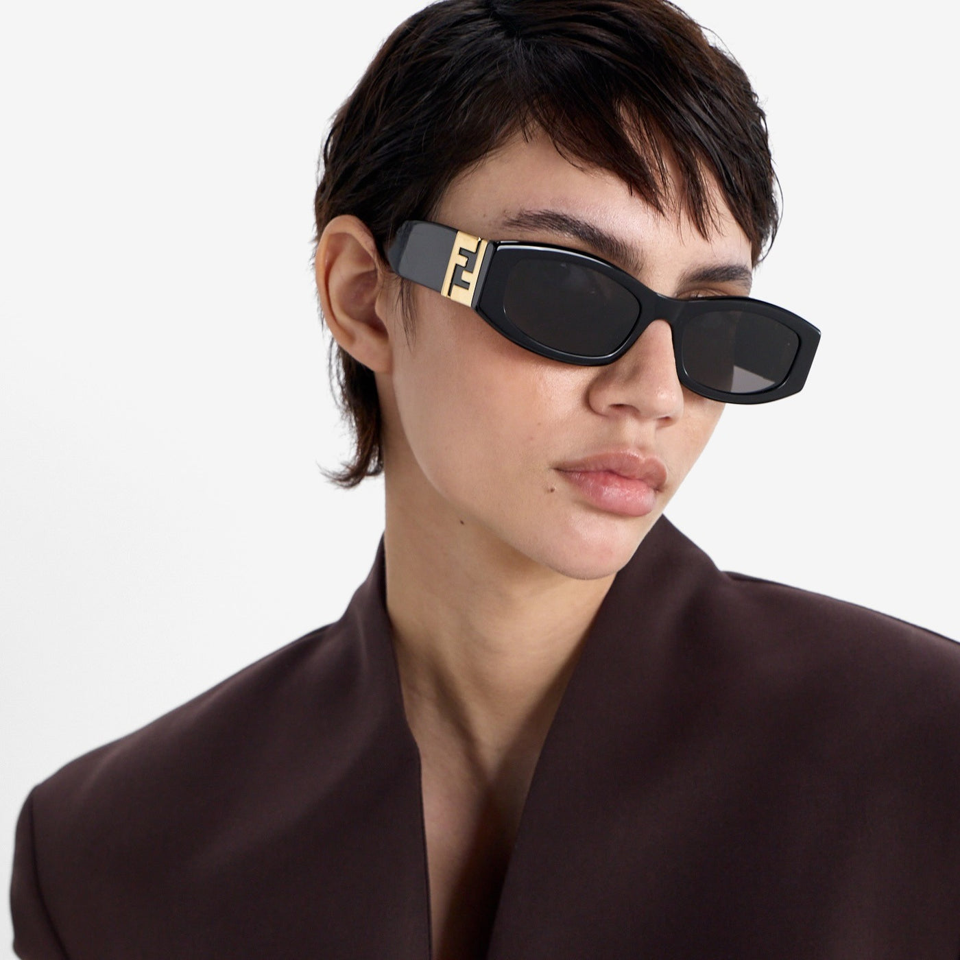 Person wearing black sunglasses with a gold logo on a white background