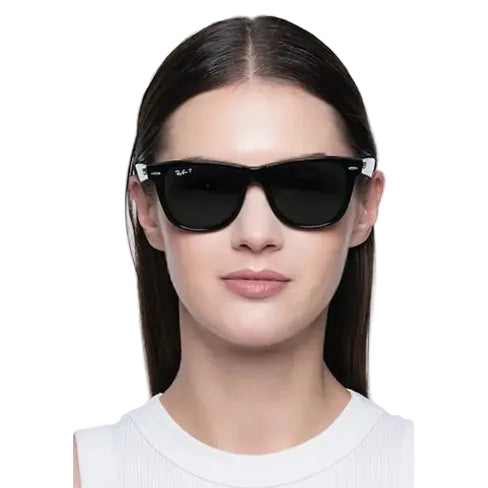 A woman with dark hair wearing black Ray-Ban sunglasses with white temple tips, shown from the chest up against a light gray background.